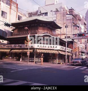 1960er Jahre, historisch, Tokio, Japan, altes japanisches Gebäude an der Ecke einer Straße in der Innenstadt der Stadt. Die traditionelle japanische Architektur ist eine Stilmischung, wobei das große geschwungene Dach ein Hauptmerkmal ist und Holz das bedeutende Baumaterial ist. Stockfoto