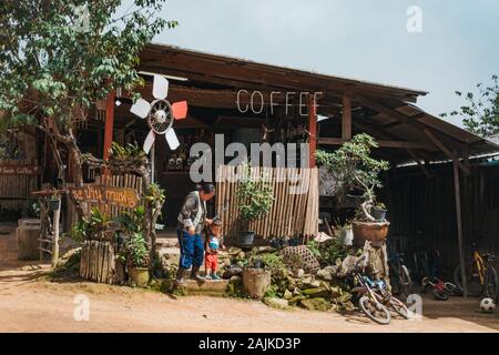 Eine thailändische Frau hilft einem Jungen Treppen an einem ruhigen, kleinen Coffee Shop in einem ländlichen Dorf auf einem Hügel außerhalb von Chiang Mai, Thailand Stockfoto