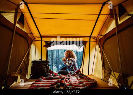 Gerne einsam nach kaukasische Frau sitzen vor einem Zelt genießen eine Tasse Tee und die wilde Natur rund um Outdoor-freie alternative Camping vacatio Stockfoto