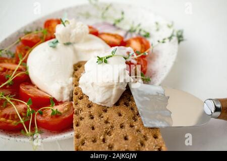 In Scheiben geschnittene frische Italienische burrata Käse mit Tomatenscheiben auf Brot auf einem weißen Hintergrund. Close Up. Selektive konzentrieren. Gesund italienisches Essen. Stockfoto