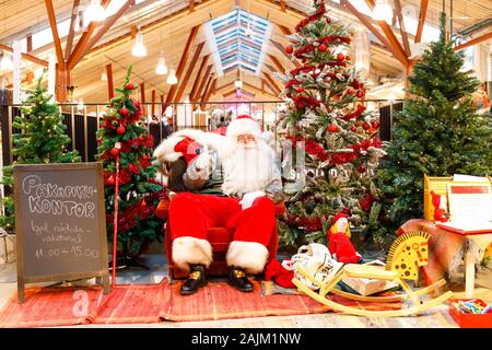 TALLINN, Estland - 22 Dezember, 2019: Santa Claus sitzt zwischen dekorierte Tannenbäume in Balti Jaam Markt bulding in Tallinn Estland im Dezember 2019 Stockfoto