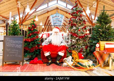 TALLINN, Estland - 22 Dezember, 2019: Santa Claus sitzt zwischen dekorierte Tannenbäume in Balti Jaam Markt bulding in Tallinn Estland im Dezember 2019 Stockfoto
