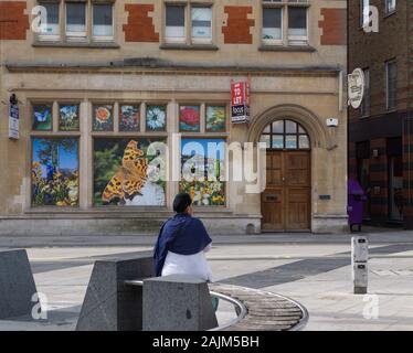 Sikh man sitzt auf einer Bank in einer Fußgängerzone von Slough. Dahinter steht die alte HSBC-Bank, jetzt "zur Miete". Fenster enthalten Blumen aus den Slough Parks. Stockfoto