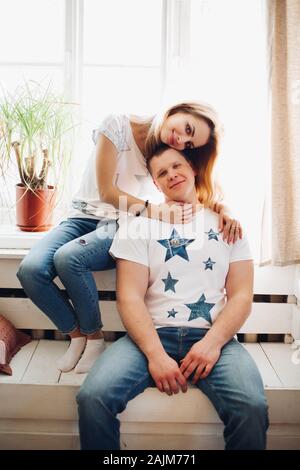 Portrait von romantisches Paar, sitzen auf den weißen Holzbank vor der großen Fenster. Freund und Freundin tragen im weißen T-Shirt und Jeans embra Stockfoto