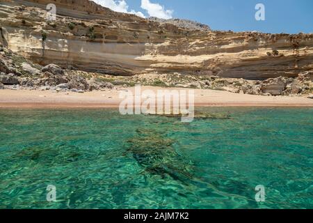 Blick von einem Motorboot auf dem Mittelmeer an der felsigen Küste mit rotem Sand Strand und klares türkisfarbenes Wasser in der Nähe von Stegna auf der Ostseite des Gr Stockfoto
