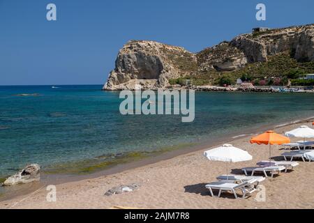 Stegna Beach auf der griechischen Insel Rhodos mit Sand, Sonnenschirmen und Boote im Hintergrund an einem sonnigen Tag im Frühjahr Stockfoto