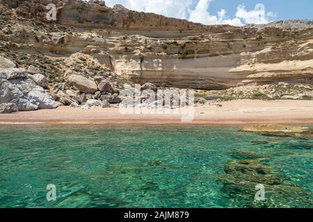 Blick von einem Motorboot auf dem Mittelmeer an der felsigen Küste mit rotem Sand Strand und klares türkisfarbenes Wasser in der Nähe von Stegna auf der Ostseite des Gr Stockfoto