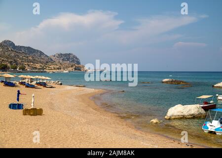 Stegna Beach auf der griechischen Insel Rhodos mit Sand, Sonnenschirmen und Boote im Hintergrund an einem sonnigen Tag im Frühjahr Stockfoto