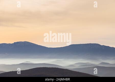 Aussichtspunkt Blick auf das Tal mit Morgennebel, der durch Sonnenaufgang aufgehellt wird, lebhaften Farben des Himmels und weit entfernten, beeindruckenden Bergschichten Stockfoto