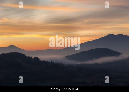 Aussichtspunkt Blick auf das Tal mit Morgennebel, der durch Sonnenaufgang aufgehellt wird, lebhaften Farben des Himmels und weit entfernten, beeindruckenden Bergschichten Stockfoto