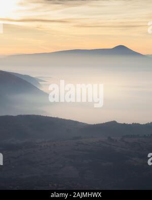 Aussichtspunkt Blick auf das Tal mit Morgennebel, der durch Sonnenaufgang aufgehellt wird, lebhaften Farben des Himmels und weit entfernten, beeindruckenden Bergschichten Stockfoto