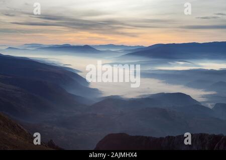 Aussichtspunkt Blick auf das Tal mit Morgennebel, der durch Sonnenaufgang aufgehellt wird, lebhaften Farben des Himmels und weit entfernten, beeindruckenden Bergschichten Stockfoto