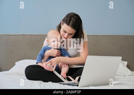 Mutter mit Zentimeter Maßband, ihr Baby zu Hause sitzen Stockfoto