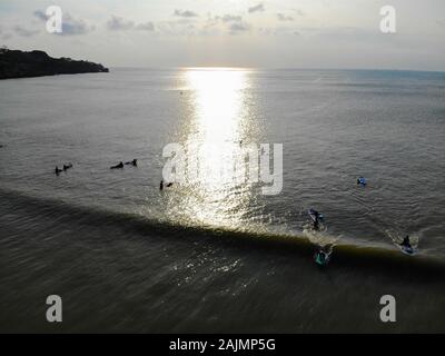 Luftaufnahme der Surfer auf ihre Pension warten die Wellen bei Sonnenuntergang, große Wellen tropical Blue Ocean, drone Ansicht von Surfer fangen die blauen Wellen, Bali, Indonesien Stockfoto