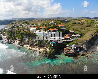 Luftaufnahme von wenig surfer Dorf an der Felswand und die Küste. Blick von oben auf die Hotels und Schwimmbad auf der Klippe in Bali. Ocean Blue Water, Ziel für Urlaub Stockfoto