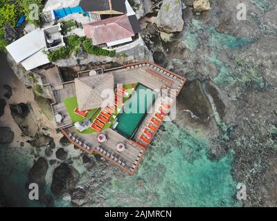 Luftaufnahme von wenig surfer Dorf an der Felswand und die Küste. Blick von oben auf die Hotels und Schwimmbad auf der Klippe in Bali. Ocean Blue Water, Ziel für Urlaub Stockfoto