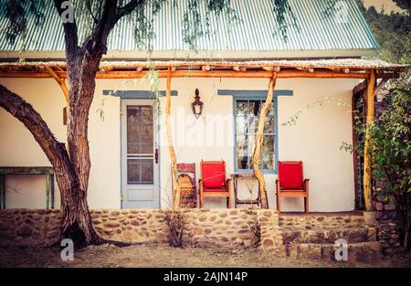 Ein Mesquite Baum in der Nähe des Pols und Baum post Veranda eines Spanischen beeinflusst Adobe Startseite mit roten Stühlen auf der Veranda in artisan Stadt TUBAC, AZ, USA Stockfoto