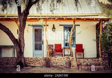 Ein Mesquite Baum in der Nähe des Pols und Baum post Veranda eines Spanischen beeinflusst Adobe Startseite mit roten Stühlen auf der Veranda in artisan Stadt TUBAC, AZ, USA Stockfoto