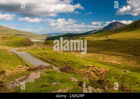 Eine Landstraße schlängelt sich durch raues Grasland an Rhyd Ddu, die Köpfe der drei Täler, unter den Bergen von Snowdnia. Stockfoto