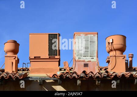 Spanische Fliesen auf der Dachterrasse mit alten kühler Sumpf, Klimaanlage, Lüftungsschlitze und Auspuffrohre alle in einem flachen Wüste Farbe gegen einen strahlend blauen Himmel Stockfoto