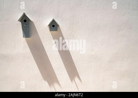 Zwei Nistkästen auf mit Beton verputzte Wand werfen lange Schatten diagonal nach unten an der Wand. Stockfoto