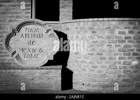 Aus zentrierten Blick auf eine traditionelle Hand geschnitzten Stein Zeichen für die Plaza Antigua de Mexico in rauen Licht gegen eine alte Adobe brick wall in Tubac, AZ Stockfoto