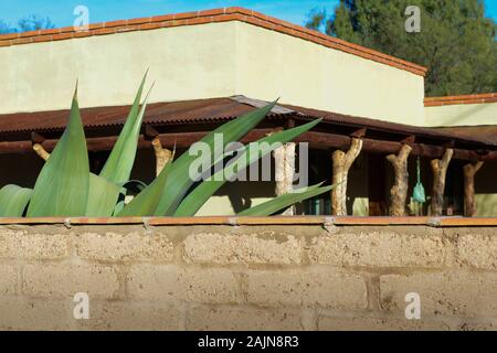 Werfen Sie einen Blick über einen adobe-Backstein Courtyard Wall des südwestlichen Home mit Baumstämmen für Support Post am Portal, von Agaven und Kakteen in Tubac, AZ umgeben Stockfoto