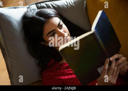 Persische Frau zu Hause lesen auf der Couch Stockfoto