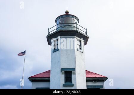 Einen historischen Leuchtturm bei bedecktem Himmel und die amerikanische Flagge im Hintergrund. Stockfoto