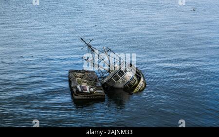 Ein teilweise versenkt Schiff, liegend auf die Seite, gegen graue Wasser in Dockton Hafen. Stockfoto