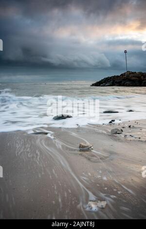 Bewegte Wellen und stürmische Wolken bei Sonnenuntergang an der Küste von Dorset, am Strand von Highcliffe, Dorset, Großbritannien Stockfoto