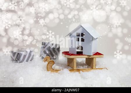 Winter Verkauf von Immobilien. Haus auf einem Schlitten und Geschenken in den Schnee. Stockfoto