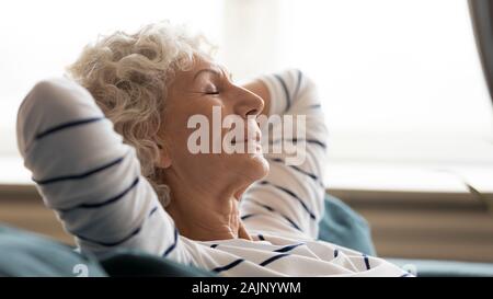 60 s Frau geschlossenen Augen, Hände hinter dem Kopf drinnen Stockfoto