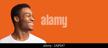 Half-Turned lächelnd afrikanische amerikanische Mann an der Suche Kopie Raum isoliert über Orange Studio Hintergrund, Panorama Stockfoto