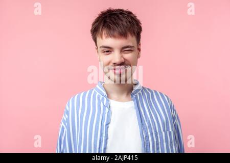 Porträt der glückliche junge braunhaarige Mann mit dem kleinen Bart und Schnurrbart in lässig-gestreiftes Hemd an Kamera winking, verspielt und positiven Gesichtsausdruck Stockfoto