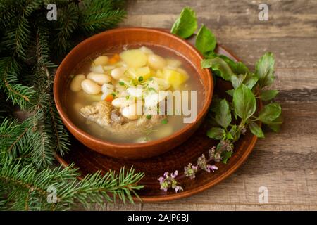 Rustikale Huhn Bohnen Suppe, russische Küche, Keramik Schüssel, grün und lila Basilikum, Holz- Hintergrund Stockfoto