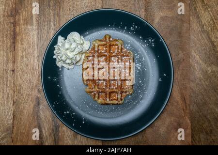 Mit hausgemachten belgischen Waffeln auf einem Teller. Mit Pulver Zucker und Sahne auf der Seite. Ansicht von oben Stockfoto