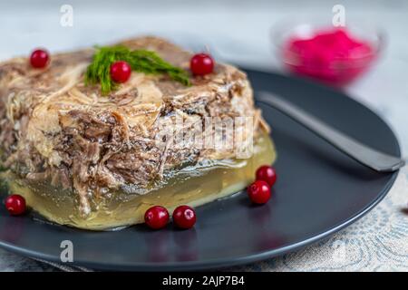 Gelee mit Fleisch, Schwein und Huhn, Aspik. Traditionelle russische Gericht, auf einem dunklen Platte, das nächste in einer Schüssel zu Meerrettich. Auf einem grauen Hintergrund unter Stockfoto
