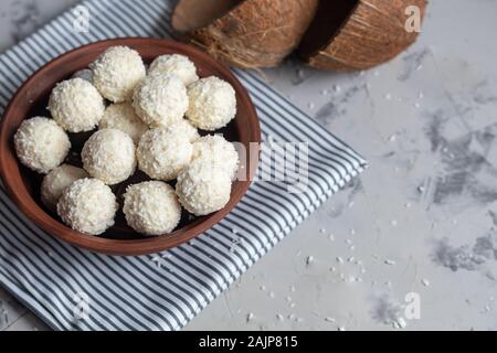 Bonbons in Kokosraspeln und frische Kokosnuss mit Leinsamen auf grauem Stein. Energie Kugeln. Kopieren Sie Platz. Stockfoto