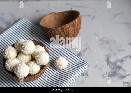 Bonbons in Kokosraspeln und frische Kokosnuss mit Leinsamen auf grauem Stein. Energie Kugeln. Kopieren Sie Platz. Stockfoto