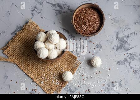 Bonbons in Kokosraspeln und frische Kokosnuss mit Leinsamen auf grauem Stein. Energie Kugeln. Kopieren Sie Platz. Stockfoto