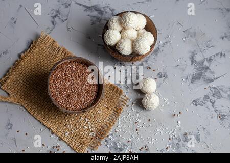 Bonbons in Kokosraspeln und frische Kokosnuss mit Leinsamen auf grauem Stein. Energie Kugeln. Kopieren Sie Platz. Stockfoto