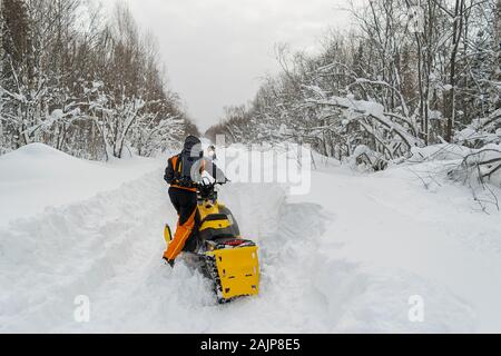 Ein Mann, ein Athlet in einem warmen Sportanzug Fahrten mit einem Schneemobil auf einer verschneiten Straße vor dem Hintergrund einer Winter wald landschaft Stockfoto