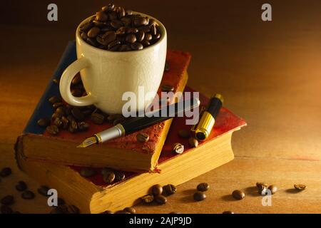 Kaffeebohne im weißen Schale und vintage Buch stapeln auf Holztisch im Morgenlicht. Stockfoto