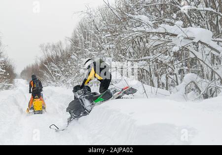 Zwei Menschen, die Athleten, die Fahrt auf Motorschlitten auf einer verschneiten Straße vor dem Hintergrund einer Winter wald landschaft Stockfoto