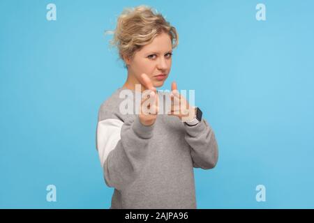 Gefährliche Frau mit lockigem Haar in sweatshirt Zeigefinger Gewehr zu Kamera und wütend suchen, bedrohlich zu töten, mit dem Ziel, Hand Pistole, vorwärts Choo Stockfoto