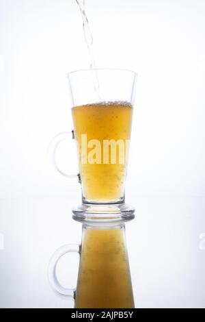 Licht unfiltrierte Bier ergossen sich in eine dampfende Tasse auf einem weißen Hintergrund mit Reflektion Stockfoto