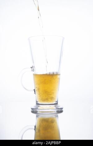 Licht unfiltrierte Bier ergossen sich in eine dampfende Tasse auf einem weißen Hintergrund mit Reflektion Stockfoto