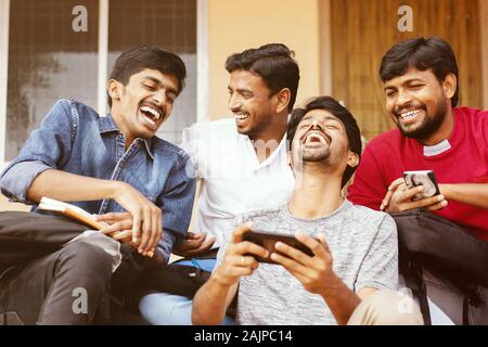 Gruppe der glückliche junge Studenten um Handy suchen laut lachend an der Universität Campus - Millennials genießen online video Inhalt oder Stockfoto