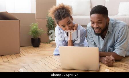 Afrikanische amerikanische Paar im Internet surfen mit Laptop auf dem Boden liegend unter Kisten nach Umzug in neues Haus. Panorama Stockfoto